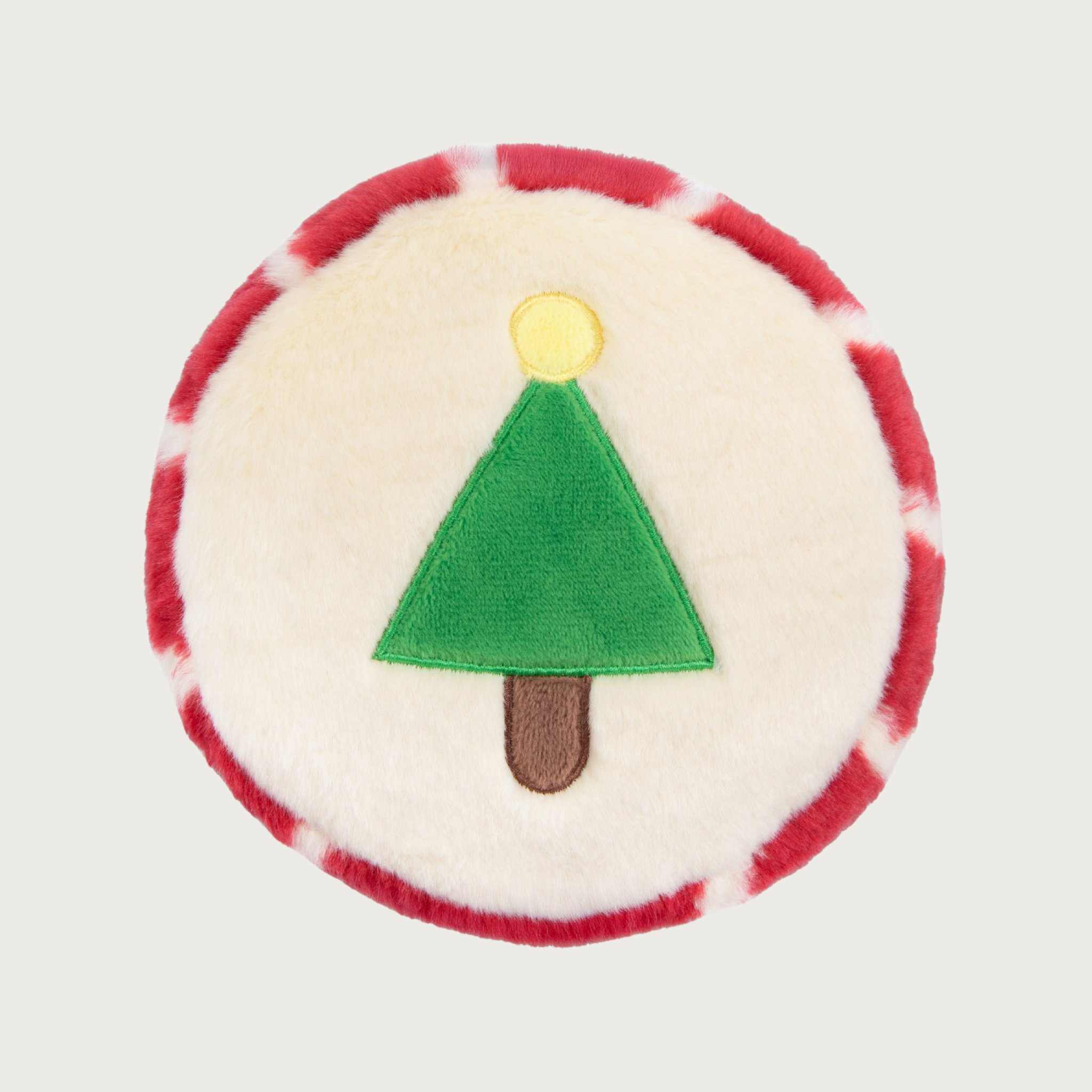 Christmas-themed, round plush dog toy. In the center is a simple green Christmas tree with brown trunk and yellow circle "star" on top. The body of the toy is cream colored, and the edge of the toy is red & cream striped.