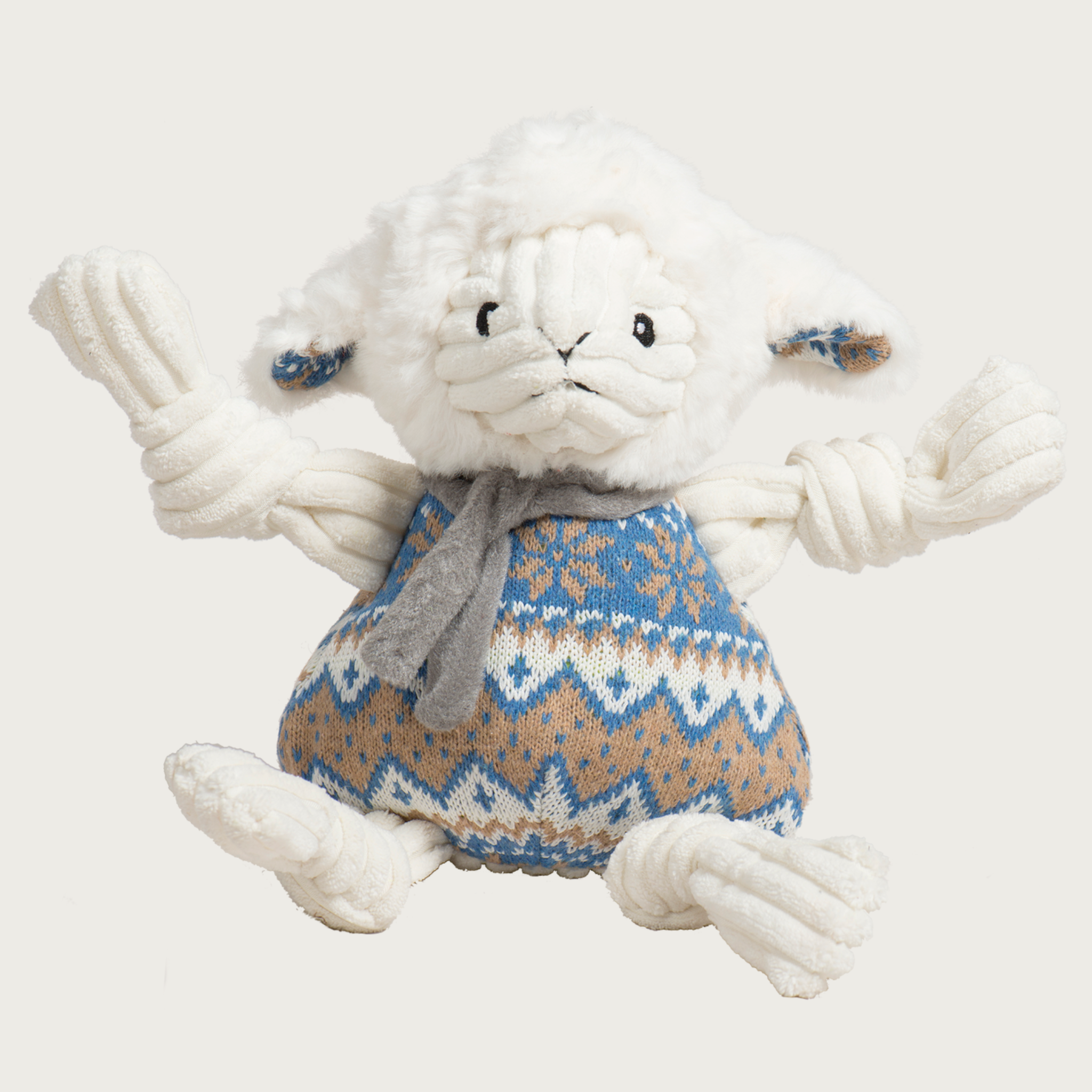 Cream colored lamb dog toy with corduroy knotted limbs and a blue, cream & tan knit on its body, resembling a Nordic print. It's also wearing a gray scarf.