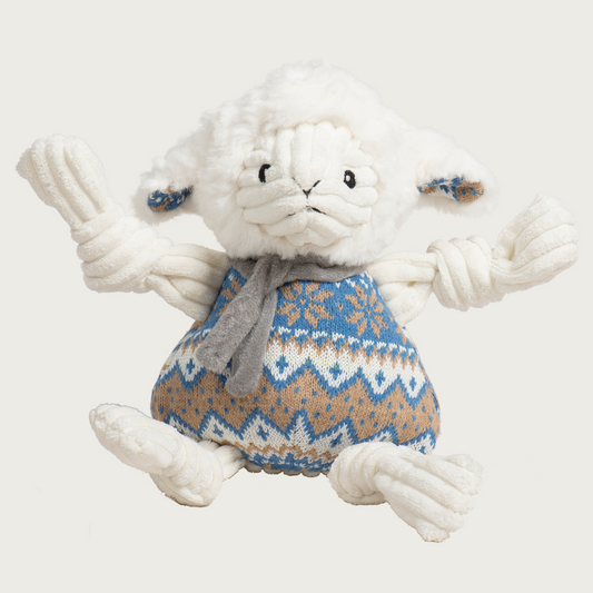 Cream colored lamb dog toy with corduroy knotted limbs and a blue, cream & tan knit on its body, resembling a Nordic print. It's also wearing a gray scarf.