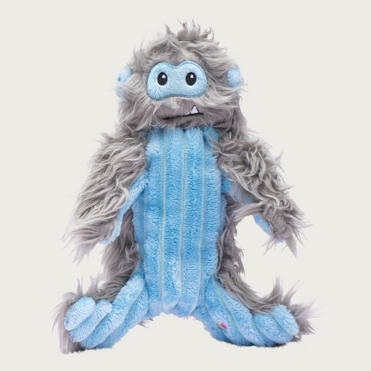 Plush dog toy resembling a hairy, abominable snowman with shaggy gray fur on its back, light blue corduroy on its front, and cute embroidered facial features.
