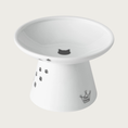 Load image into Gallery viewer, Wide, raised, white porcelain cat food bowl with black paw print design trailing up the side, and a small black cat head silhouette in the center.