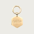 Load image into Gallery viewer, Hexagon shaped, brushed gold Tailr Pet ID Tag, with matching circular ring to attach to a pet's collar. Tag is engraved with the word "tailr".