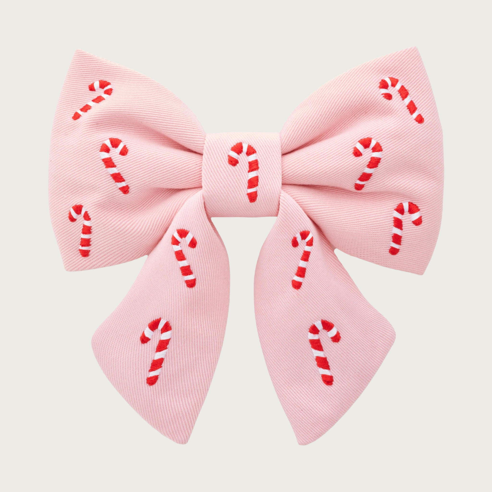 Christmas-themed, pale pink dog lady bow with small red & white striped candy cane accents, by The Foggy Dog. Looks like a hair bow for a person, with the center bow tie and ends hanging down.
