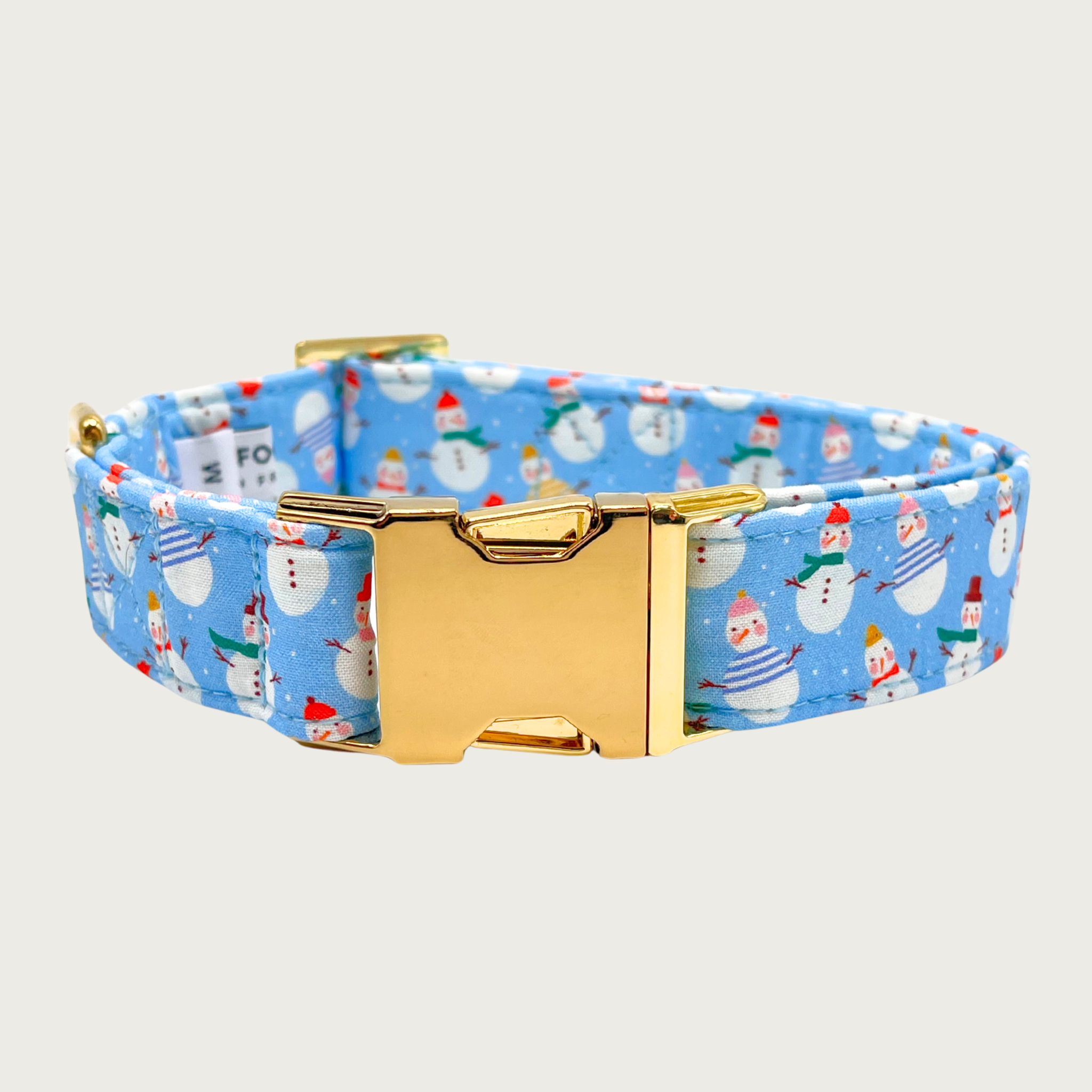 Light blue dog collar with snowman print, with tiny white dots that look like snow. The snowmen are all wearing different colored scarves and hats. Gold tone metal buckle and D-ring.