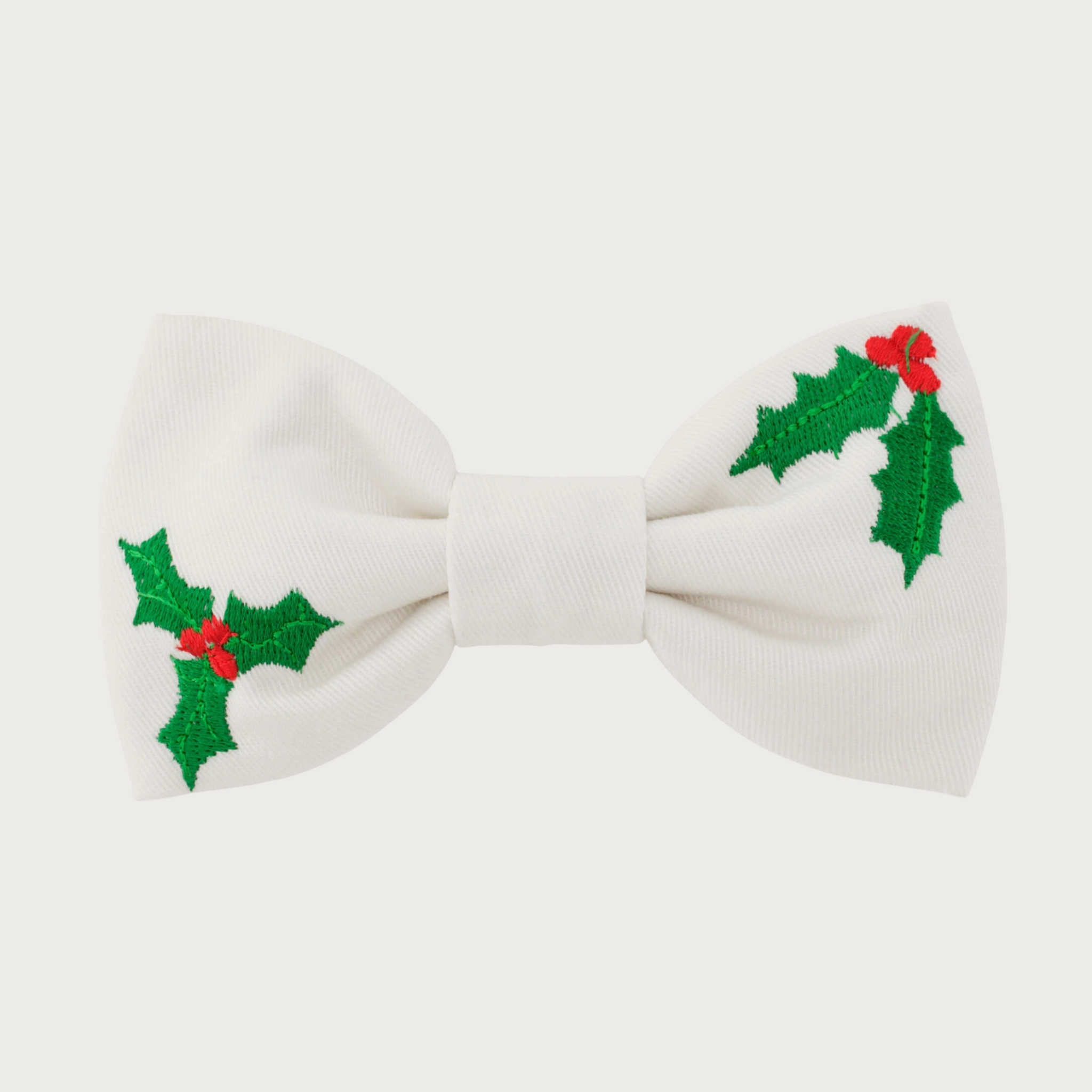 Christmas-themed, white dog bow tie by The Foggy Dog with embroidered green holly leaves & red berry accents on top right and bottom left of the tie.