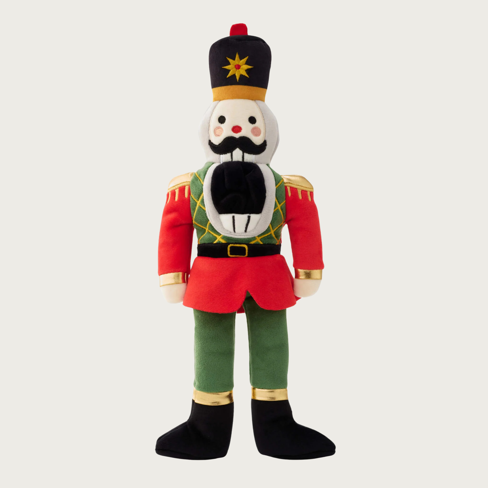 Christmas-themed plush dog toy in the shape of a nutcracker soldier, wearing a red, green, black and gold uniform and hat, with embroidered facial details and wide open mouth.