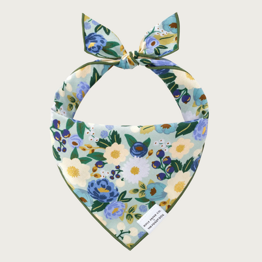 Floral patterned dog bandana in shades of blue, green, and beige, on a pale green background.