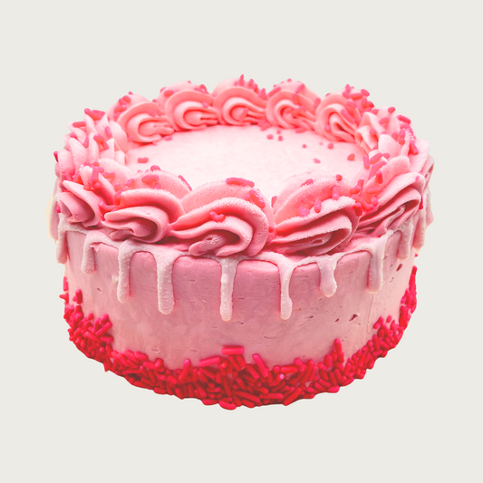 A pink colored dog birthday cake with piped frosting and drip accent, with sprinkles in various shades of pink.