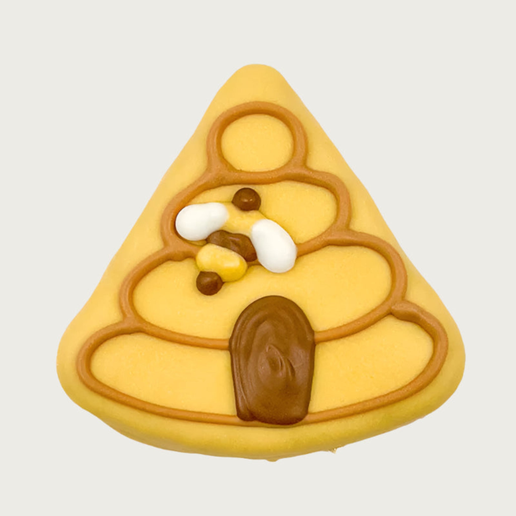 Triangular shaped dog cookie, decorated to look like a bee hive. It has a yellow coating, with hive design in tan and brown icing, with a flying bee.