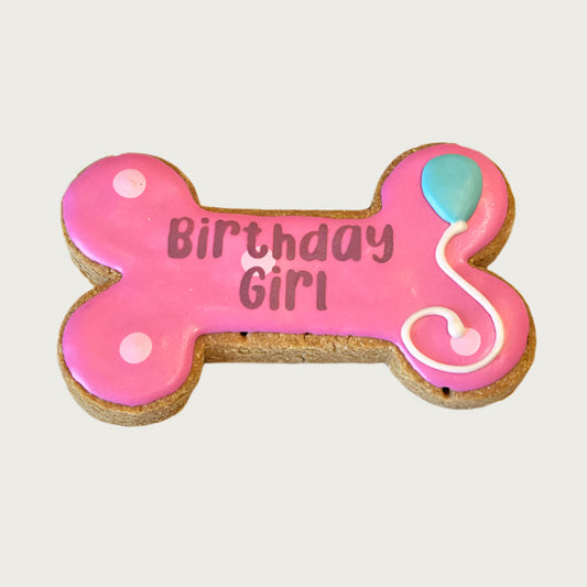 Dog bone-shaped cookie with 'Birthday Girl' text and balloon design on a pink background.