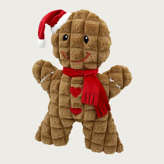 Textured waffle-style plush gingerbread man dog toy wearing a Santa hat and red scarf. Embroidered details include a cute smiley face, two heart-shaped buttons, and white "icing" squiggle on each arm.