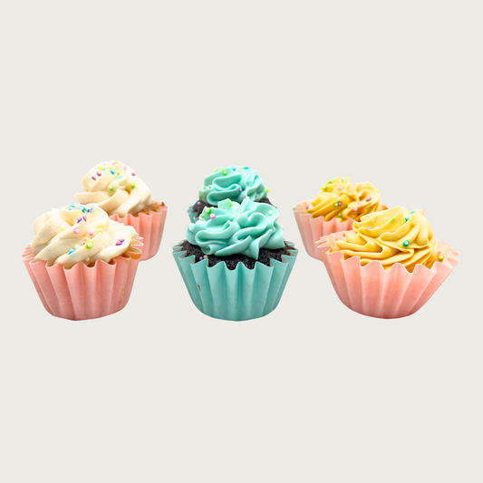 Six mini cupcakes with ivory, blue, and yellow frosting and multicolored pastel sprinkles, in pink or pale blue cupcake wrappers.
