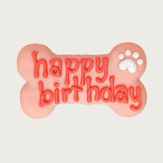 Pink bone-shaped dog cookie with 'happy birthday' text in darker pink, with white paw print accent.