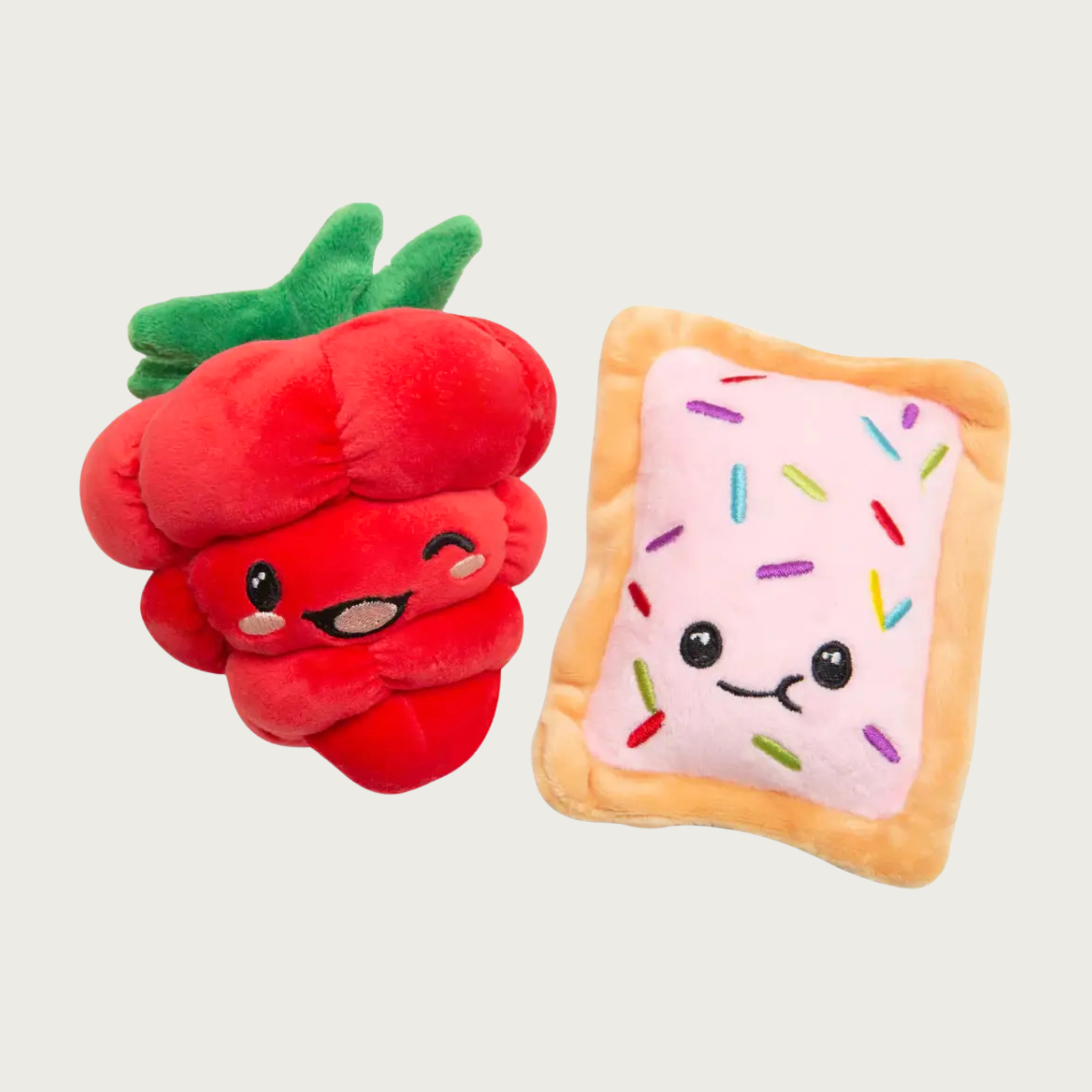 Two plush dogs toys side by side. One looks like a red raspberry, the other like a light pink frosted pop tart with multicolored sprinkles. Facial and sprinkle details are embroidered.