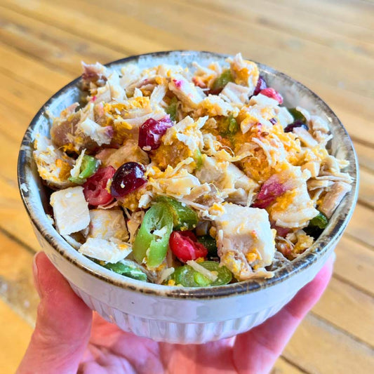 A bowl of Turkey Topper pet food topper featuring pieces of turkey, mashed sweet potatoes, green beans, and cranberries mixed together.