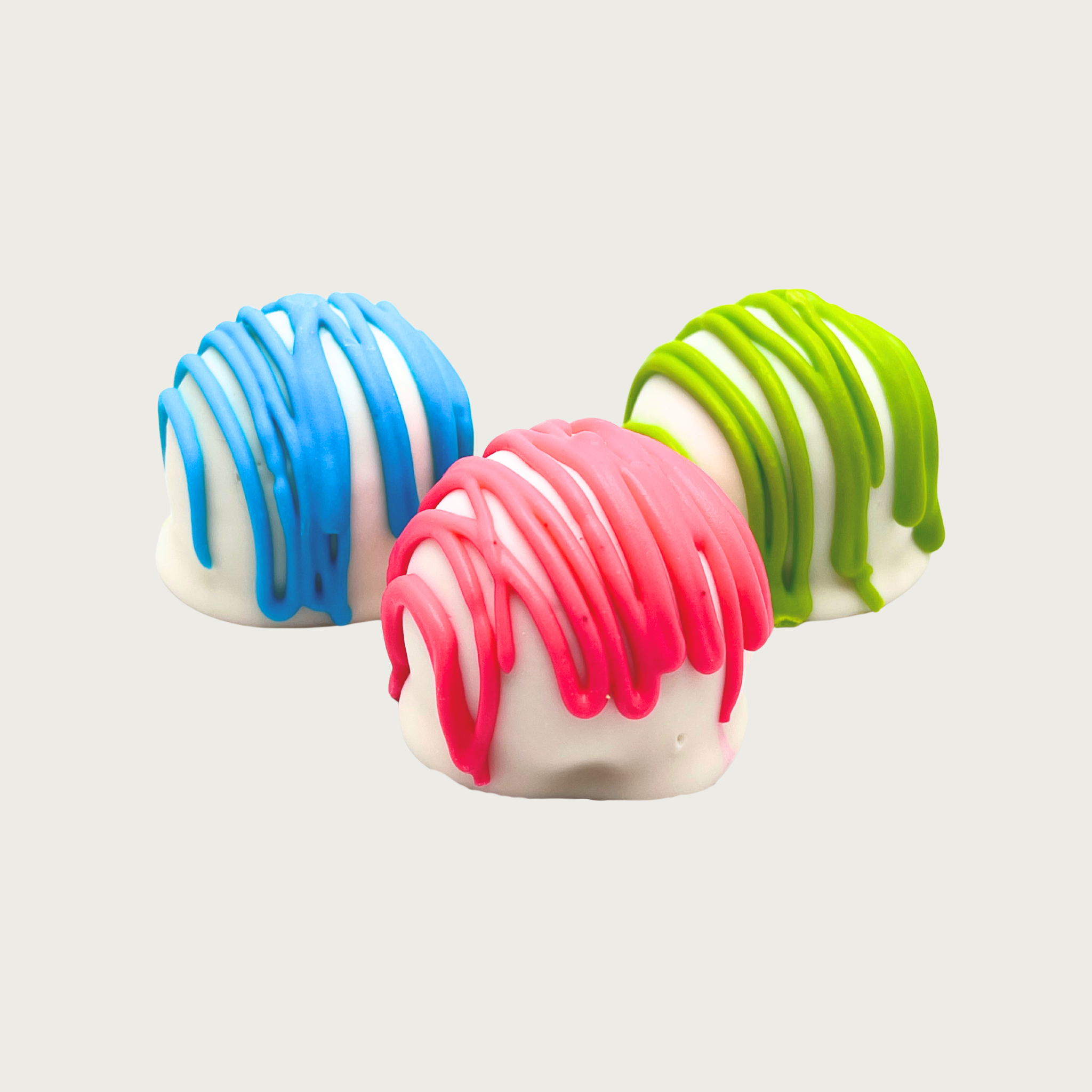 Three rounded truffle-shaped dog treats with white base and different colored drizzle (blue, pink, or green).