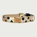 Load image into Gallery viewer, Creamy beige dog collar with large black polka dots, with a subtle, muted black swirl pattern behind the dots. Black plastic buckle and brass D-ring.
