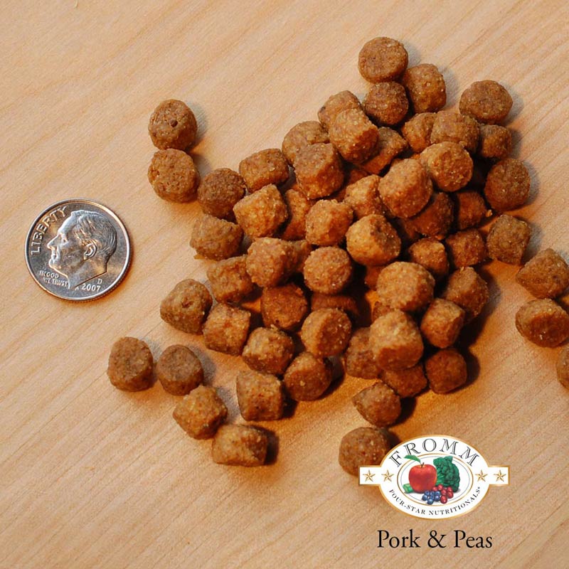 A close-up image of a handful of dry Pork & Peas kibble pieces, next to a dime for size comparison. About 3 of the pieces would fit into the area of the dime. They are small, and about the size and shape of a pencil eraser.