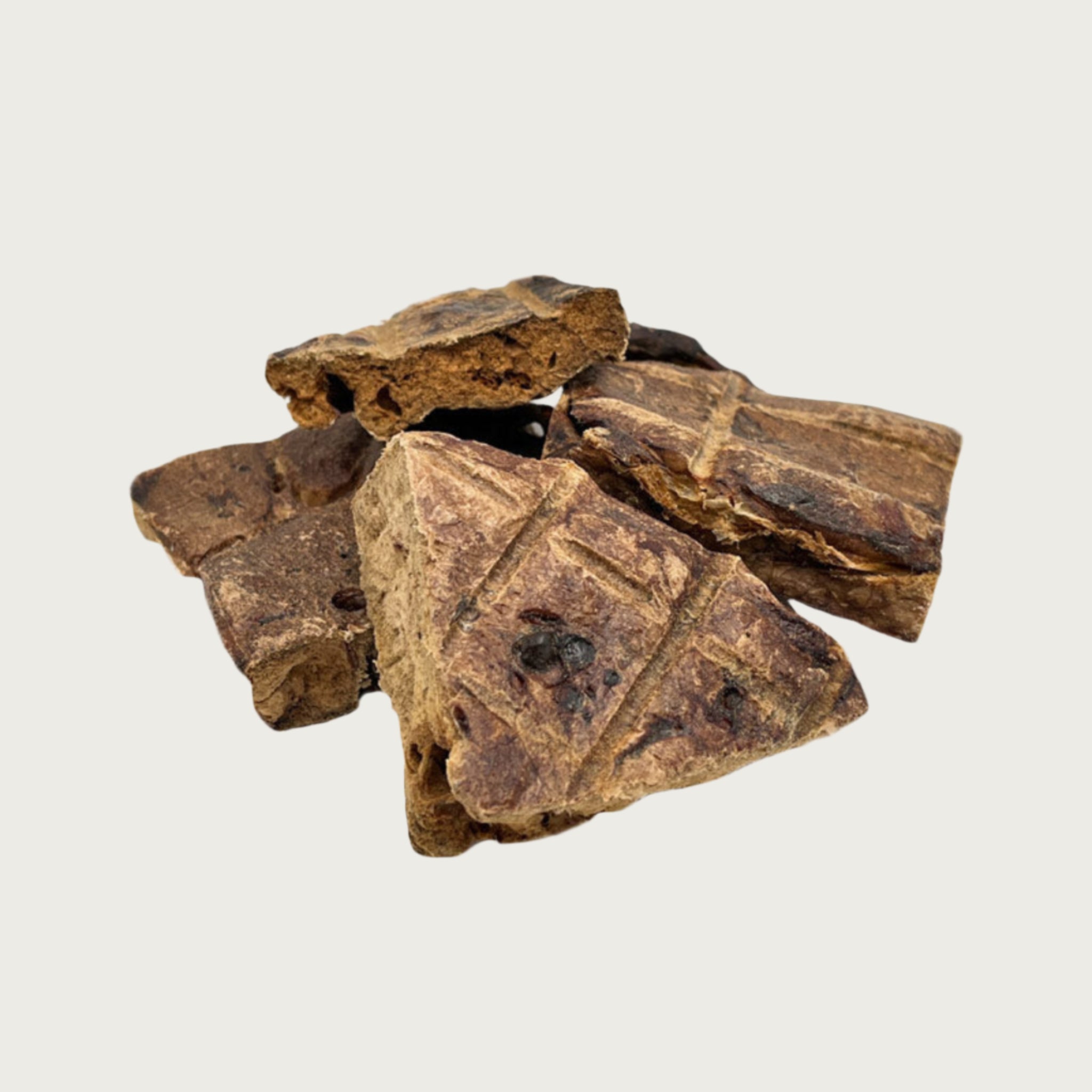 Closeup photo of a small pile of Wet Nose Buff Puffs dog treats. Product is varying sizes of square shaped, brown treats, ranging from approximately 2" - 4" wide.