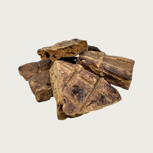 Closeup photo of a small pile of Wet Nose Buff Puffs dog treats. Product is varying sizes of square shaped, brown treats, ranging from approximately 2" - 4" wide.