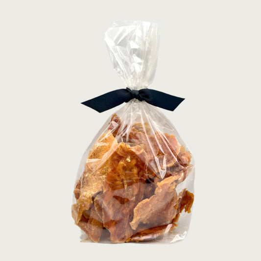 8 oz clear cellophane bag of Wet Nose exclusive Chicken Strips dog treats, tied with black ribbon. Inside are strips of chicken tenders, that are pale orangey-tan in color.