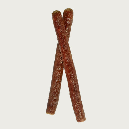 Closeup of two Wet Nose Duck Stick treats side by side. They are reddish-brown in color, and have a slightly bumpy texture.