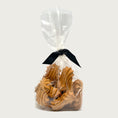 Load image into Gallery viewer, 10 oz clear, cellophane bag of Wet Nose exclusive, Goobers dog treats, tied with black ribbon. Visible inside are 3" long, tan cookies with swirl texture on top.
