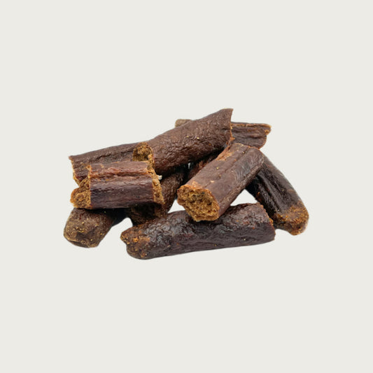 A close-up photo of a small stack of Wet Nose Misfit Duck Sticks dog treats. They are reddish brown in color about 2" long, with a slightly crumbly looking texture.