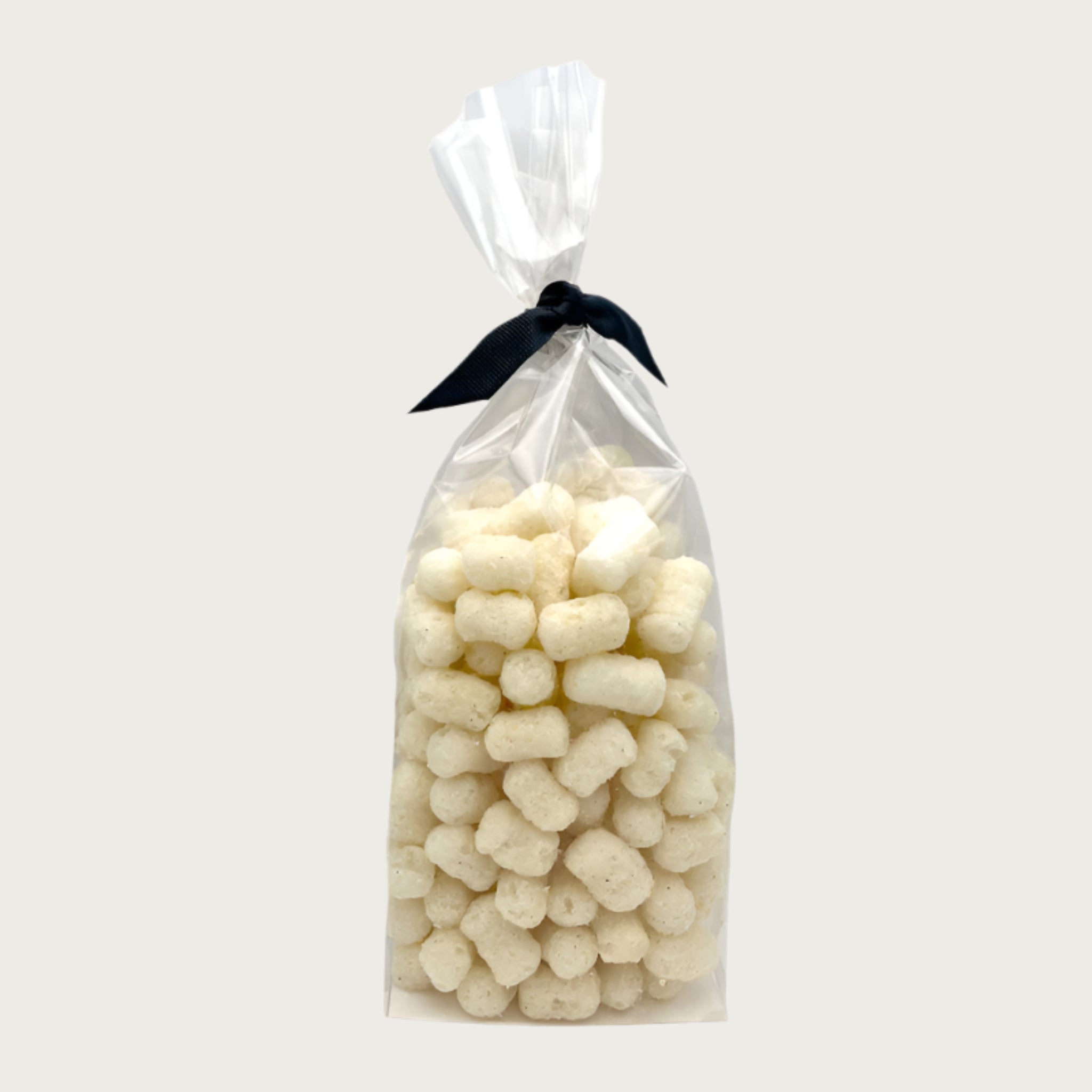 4 oz clear cellophane bag of Wet Nose exclusive Pooch Puffs dog treats, tied with black ribbon. Treats inside are ivory colored, and look like small tater tots.