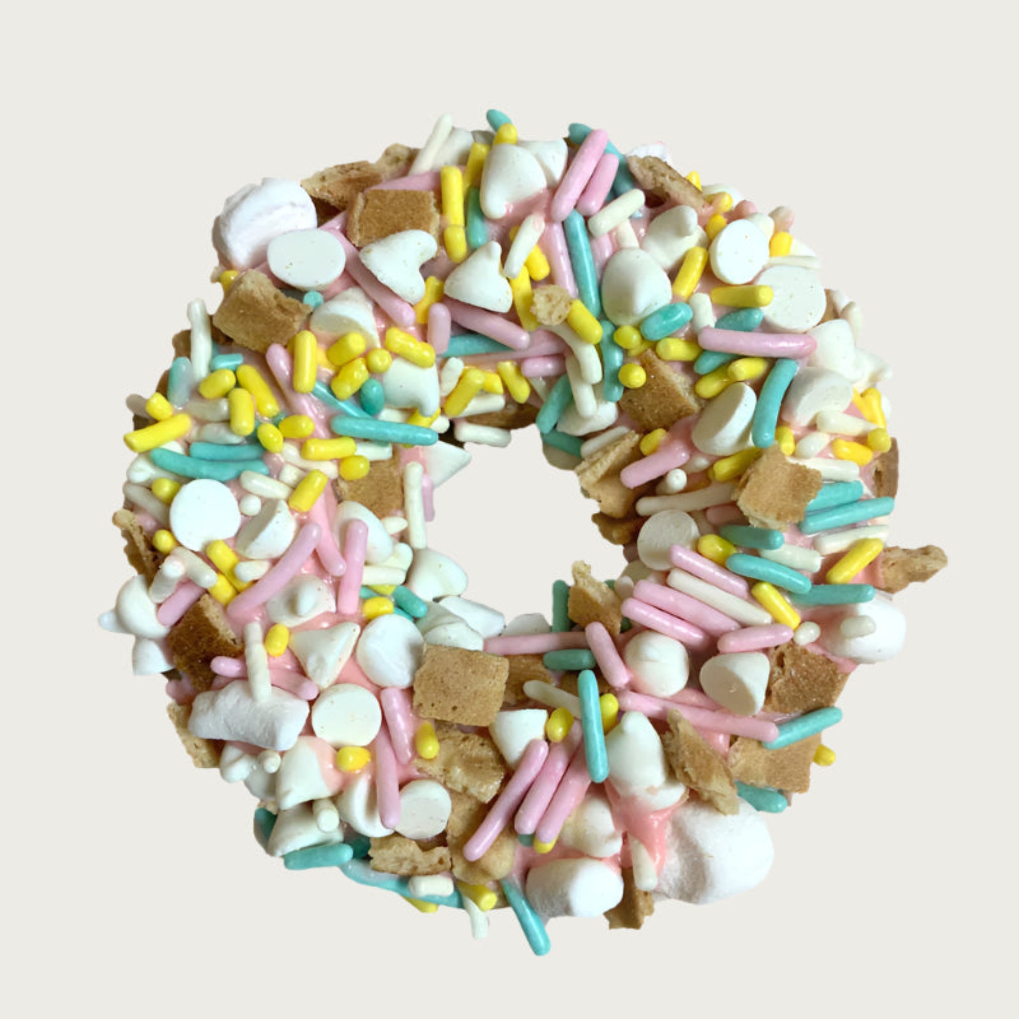 Thick, donut-shaped dog cookie decorated with pastel sprinkles, mini-marshmallows, and waffle cone pieces.