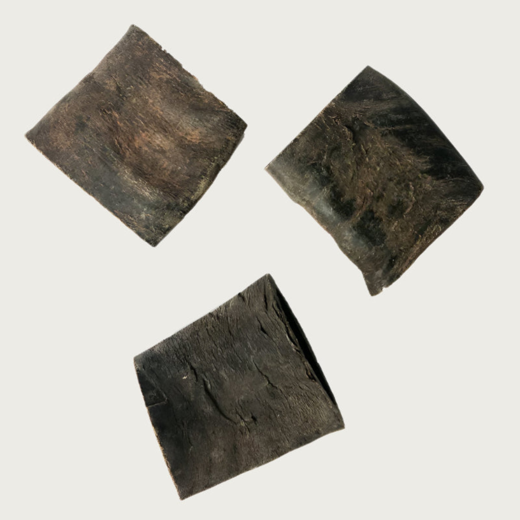 Three cut water buffalo horns dog chews to show texture and color variation. They are square shaped, and dark charcoal gray in color, with a rough texture.