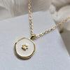 Simple gold chain necklace with a subtly irregular, round shaped pendant. Pendant is trimmed in gold, with a small gold paw print at the center. Pendant background is creamy white enamel.