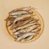 A wooden plate full of Freeze-Dried Capelin Fish from Arya! Sit. Overhead view, to show full detail. 4"-5" long fish are whole, and look similar to dried smelt. 