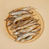 A wooden plate full of Freeze-Dried Capelin Fish from Arya! Sit. Overhead view, to show full detail. 4"-5" long fish are whole, and look similar to dried smelt. 