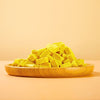 Closeup, side view of Arya! Sit Freeze-Dried Pumpkin Yogurt bites piled onto a wooden plate. They are pale orange, square to rectangular shaped cubes, about 1/2" to 1" long.