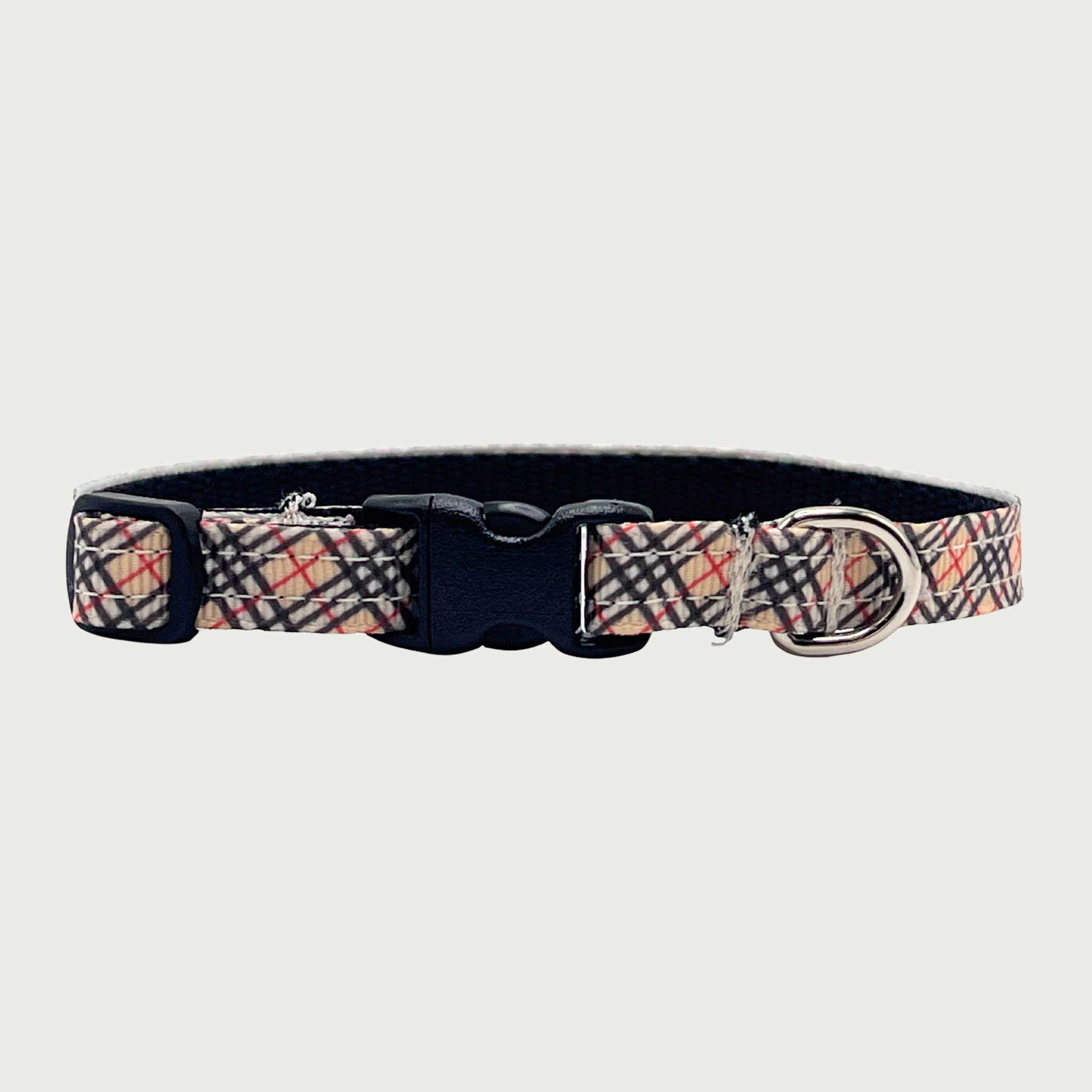 Skinny dog collar with Burberry-style red, black, and tan plaid pattern. Has a small silver D-ring, black nylon inner webbing and black plastic buckle.