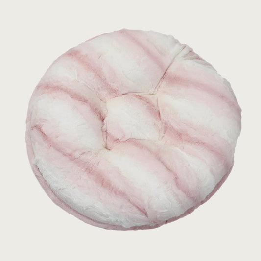 Round, plush pet bed made with faux fur in shades of pink and cream in a subtle striped pattern.