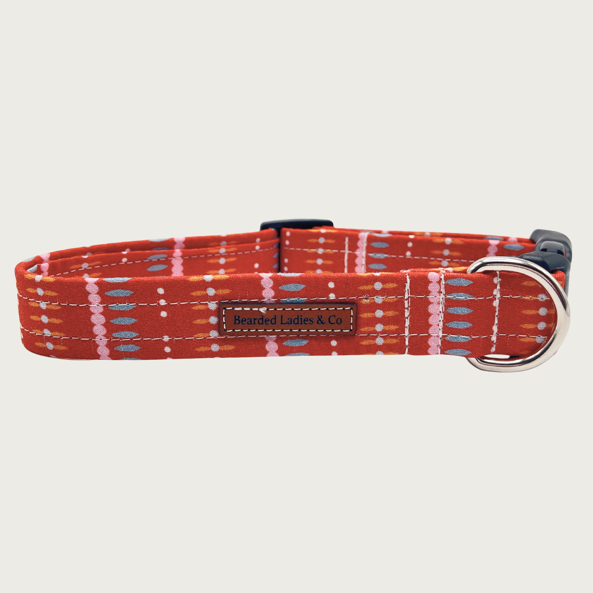 Reddish-orange dog collar with subtle dot & dash vertical striped pattern in pale pink, blue, orange, and white, with black plastic hardware and silver metal D-ring.