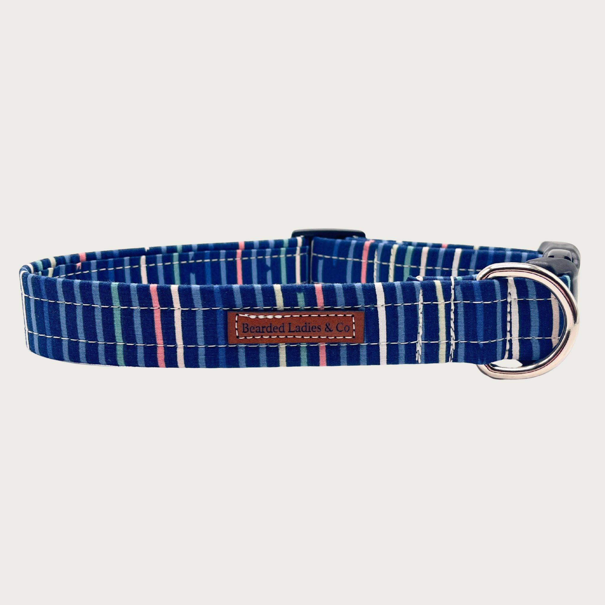 Navy blue dog collar with simple, muted vertical stripes in shades of pink, white, green, and blue, with black plastic hardware and silver metal D-ring.