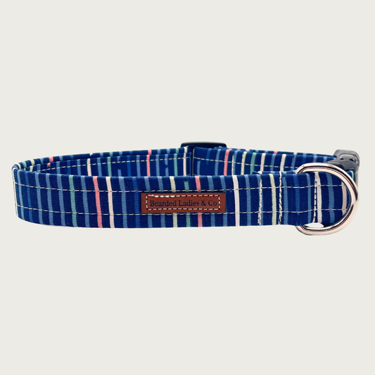 Navy blue dog collar with simple, muted vertical stripes in shades of pink, white, green, and blue, with black plastic hardware and silver metal D-ring.