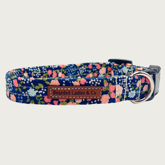 Navy blue dog collar with a multicolor simple floral print in shades of peach, pink, light blue and green, with black plastic hardware and silver metal D-ring.