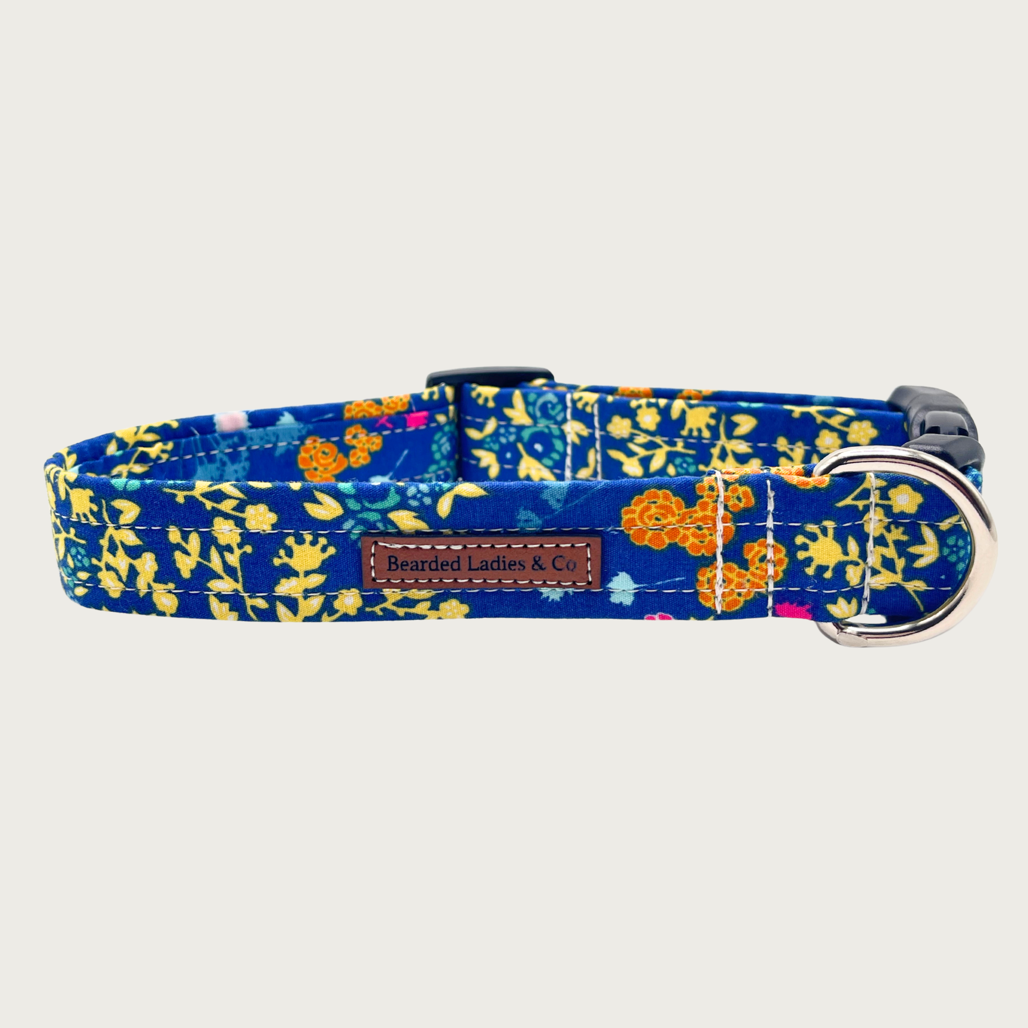 Floral-patterned dog collar with a royal blue background, and assorted wildflower print in shades of pale yellow, orange, light blue, and hot pink. Black plastic hardware and silver metal D-ring.