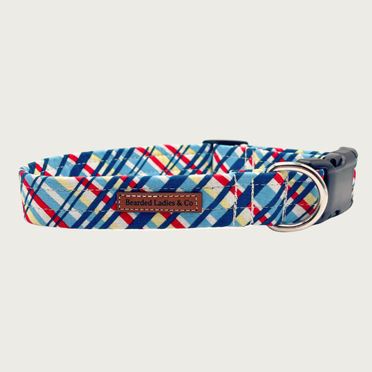 Criss-cross style plaid dog collar in shades of blue, yellow, white, and red. Black plastic hardware and silver metal D-ring.