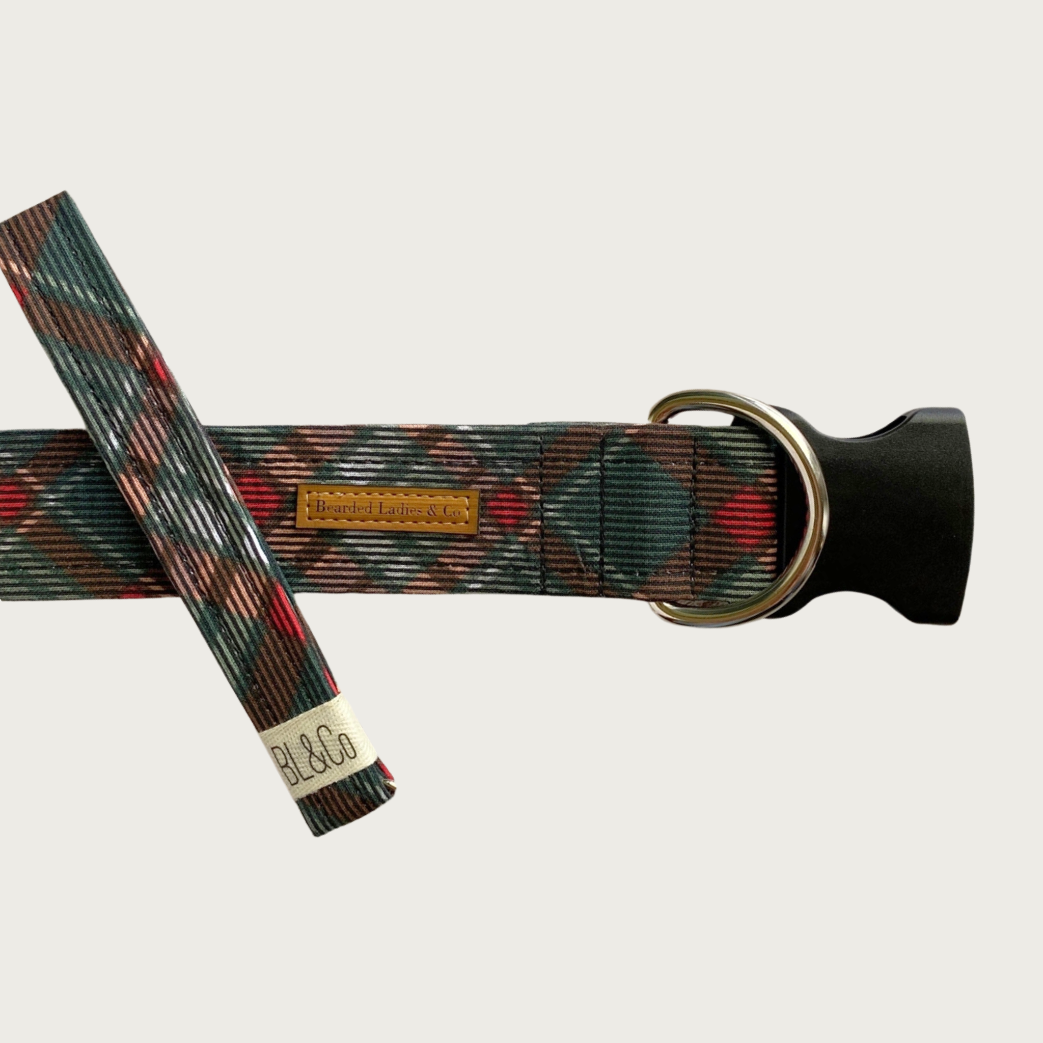 Criss-cross plaid patterned dog collar featuring darker shades of gray and red. It has a black plastic clip and silver toned D-ring. A smaller, thinner collar in the same design is leaning on the left side of the larger one, which is the focal point of the image.