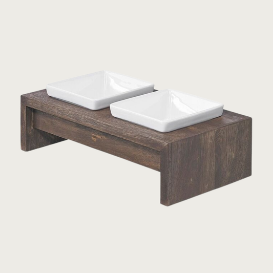 Small double bowl, elevated dog feeder. Stand is a rich dark brown wood, in a simple rectangular design. With 2 square white ceramic bowls.