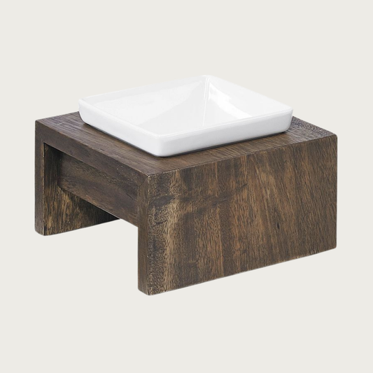 Small single bowl, elevated dog feeder. Stand is a rich dark brown wood, in a simple square design. Square white ceramic bowl in center.