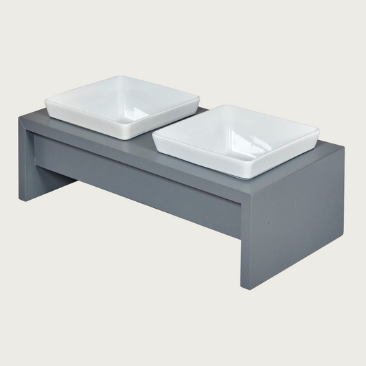 Double bowl, elevated dog feeder. Stand is a medium grey color, in a simple rectangular design. Square white ceramic bowls in center.