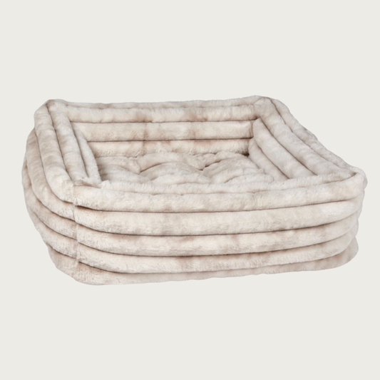 Faux fur plush rectangular pet bed with bolsters & tufted center cushion, in muddled cream & light beige tones. It features a horizontal ridged texture.