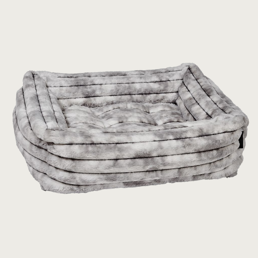 Faux fur plush rectangular pet bed with bolsters & tufted center cushion, in muddled gray & white tones. It features a horizontal ridged texture.