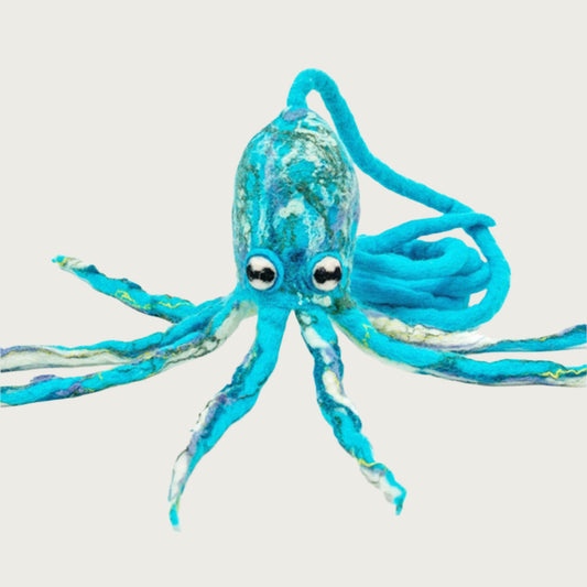 Wool octopus toy propped up by its legs that are all splayed out. Tether is attached to its head and coiled behind it. Its color is marbled tones of aqua blues, cream and green